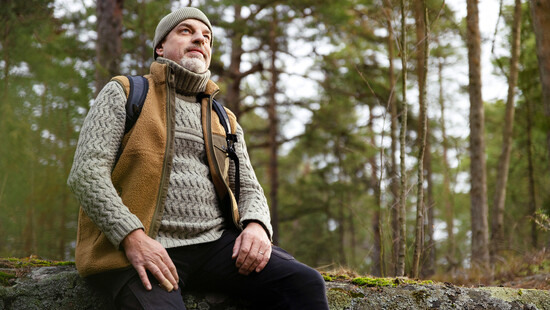 Mies istuu kalliolla metsässä