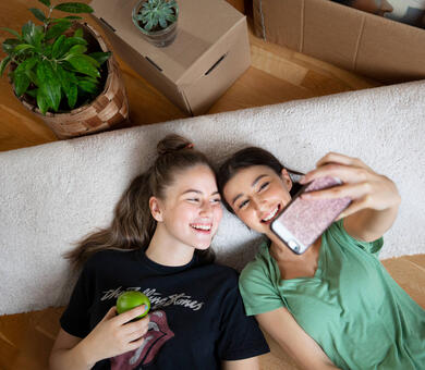 Kaksi nuorta naista selällään lattialla ottamassa selfietä
