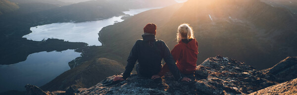 Mies ja nainen istuvat vuoren rinteellä ja katsovat vesimaisemaa